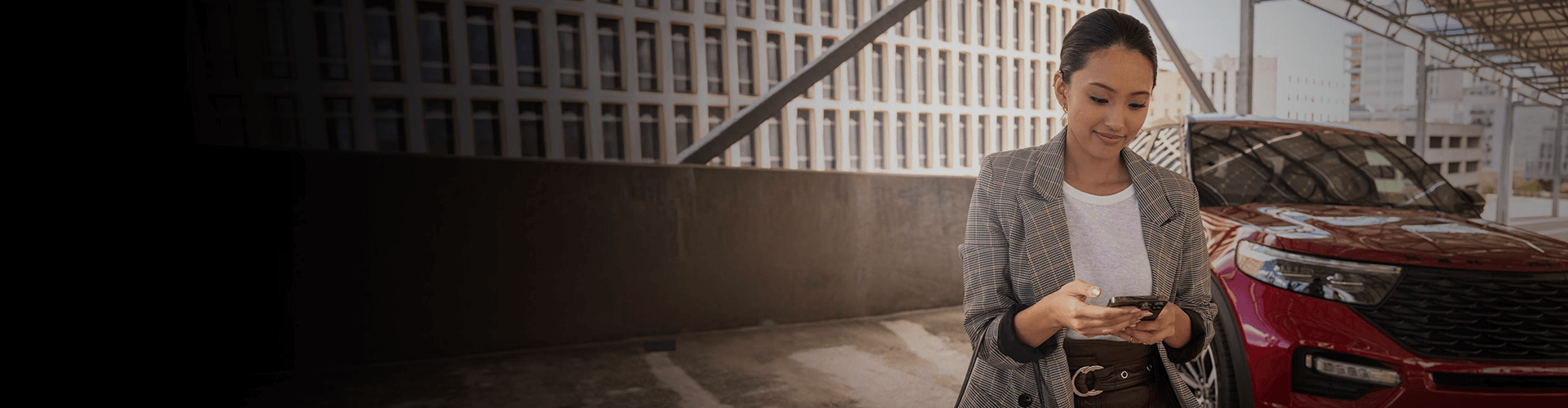 Woman using the Ford app next to a red Ford SUV in a parking garage.