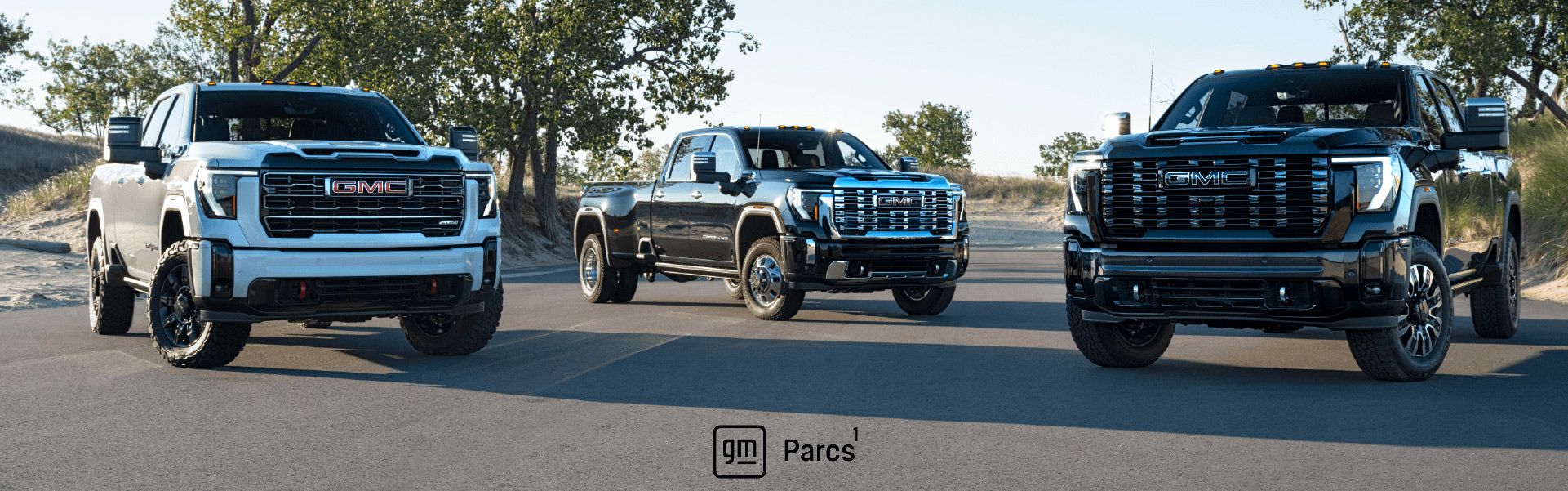 Trois camions GMC Sierra Heavy Duty stationnés sur une route. Le logo GM Parcs figure en bas au centre.