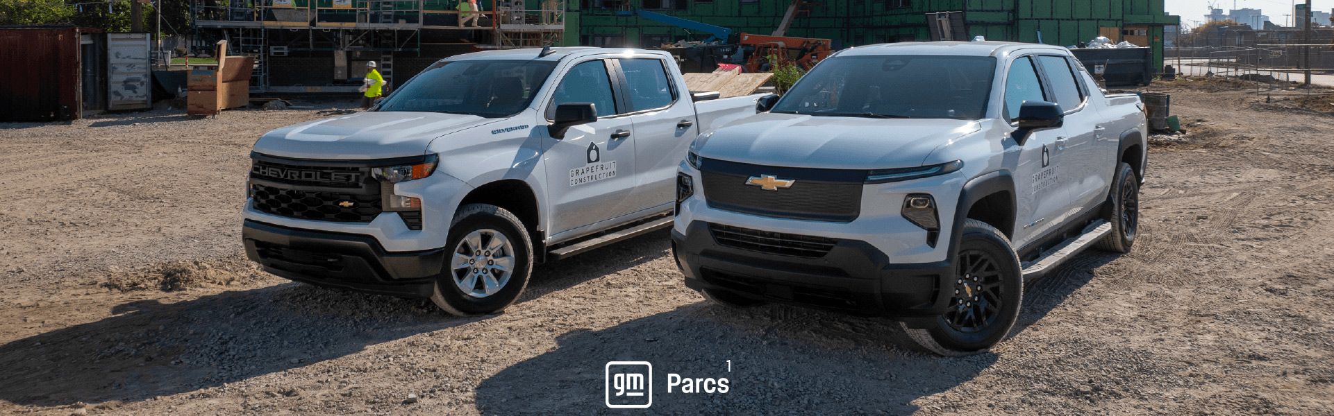 Two white Chevrolet pickup trucks parked on a dirt construction site with the GM Parcs logo at the bottom center.
