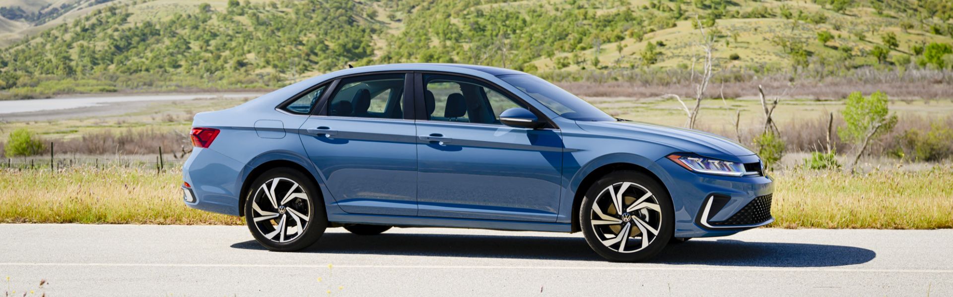 Side view of the 2026 Volkswagen Jetta in blue parked on a scenic road.