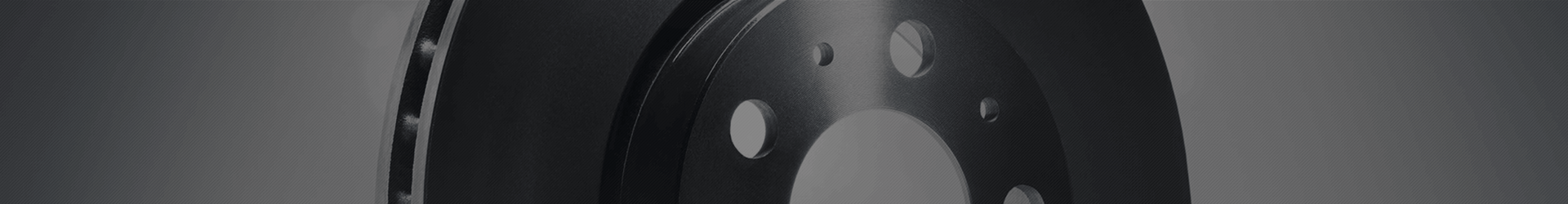 Close-up of a dark metal car brake rotor (or disk), showing the ventilation holes.