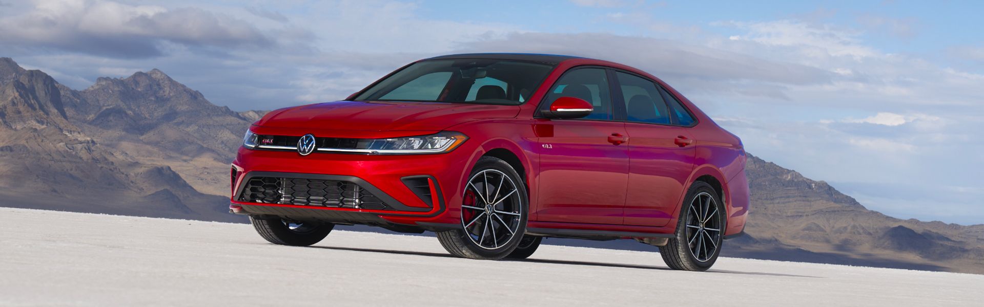 Front three-quarter view of the 2026 Volkswagen Jetta GLI in red, parked on a salt flat with mountain backdrop.