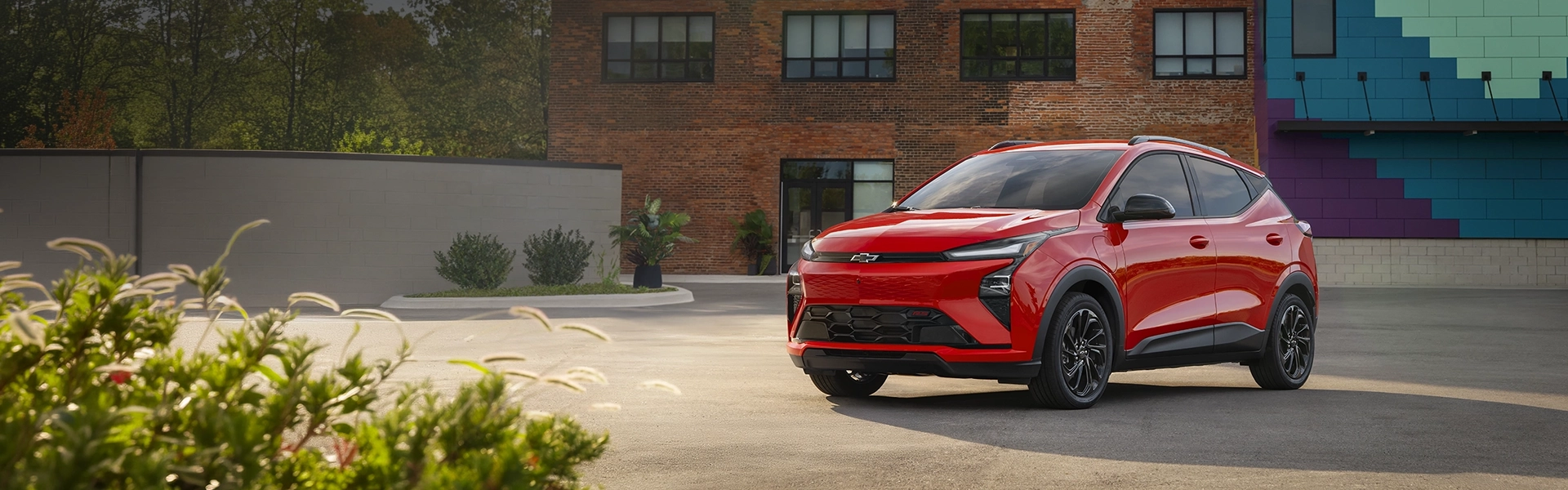Red Chevrolet Bolt EV parked in front of a brick building.