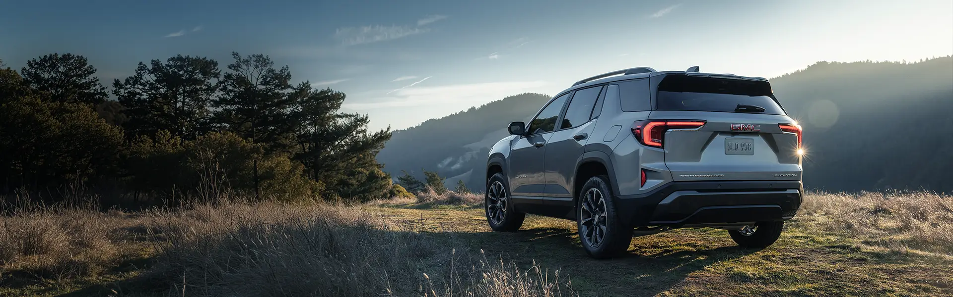 SUV GMC Terrain gris stationné dans un champ au coucher du soleil.