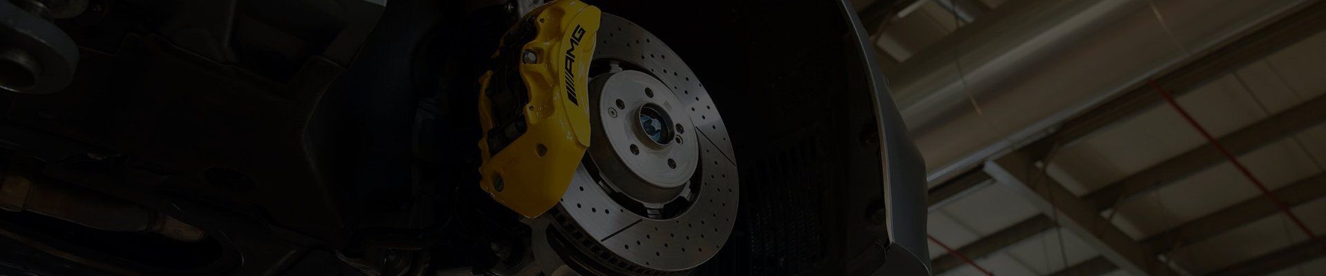 Gros plan sur un disque de frein perforé et un étrier jaune AMG sous une voiture.