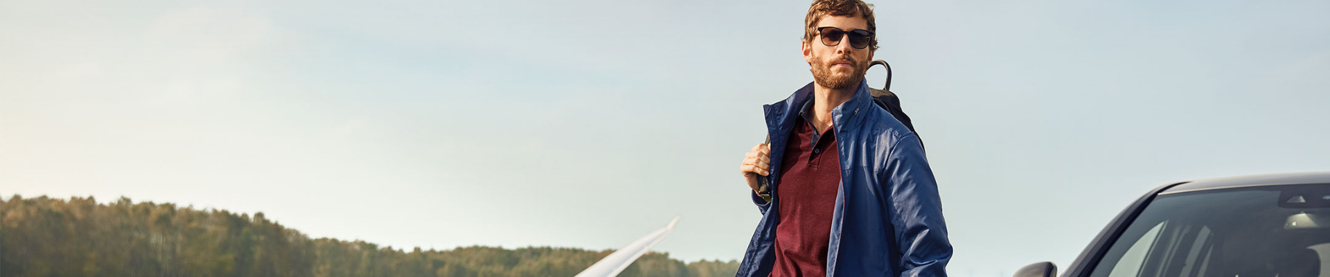 Homme en veste bleue et lunettes de soleil près d'une voiture