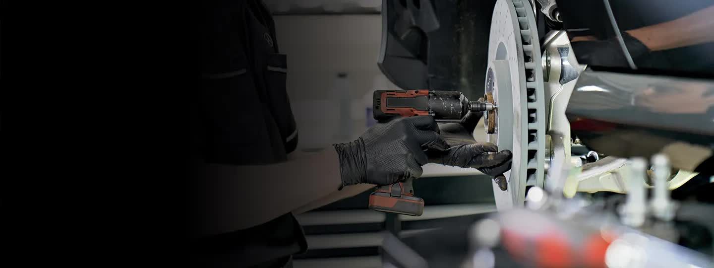 Mechanic using an impact wrench on a car brake disc.