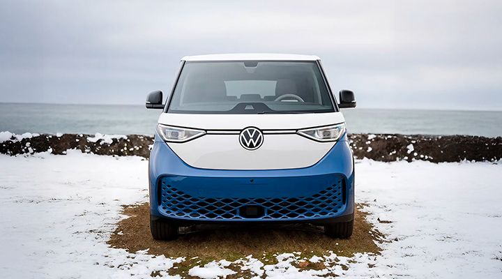 Vue de face d'une fourgonnette électrique Volkswagen ID. Buzz bicolore bleu et blanc, garée sur un terrain enneigé face à la mer.