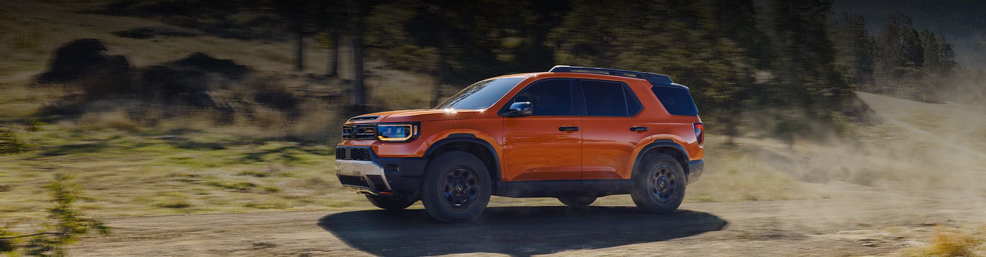 Un Honda Passport TrailSport orange roulant rapidement sur un sentier de terre avec des collines poussiéreuses en arrière-plan.