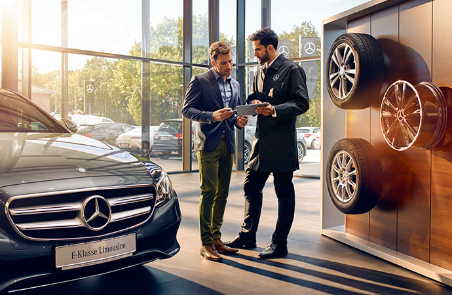 Un conseiller et un client discutent dans un showroom à côté d'un présentoir de pneus et d'une Mercedes-Benz Classe E.