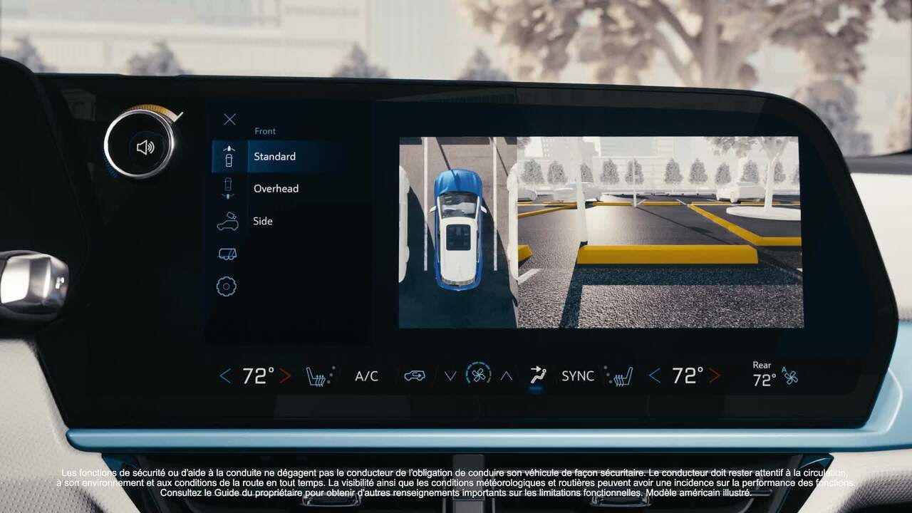Le grand écran d'infodivertissement central d'une Chevrolet Equinox EV affiche une vue de caméra à 360 degrés d'une voiture bleue et blanche garée sur un parking, avec des options pour les vues de caméra « Avant », « Standard », « Vue du dessus » et « Côté » sur la gauche. Les réglages de la climatisation sont visibles sous l'écran. Un texte en bas décrit les fonctions de sécurité en français et en anglais.