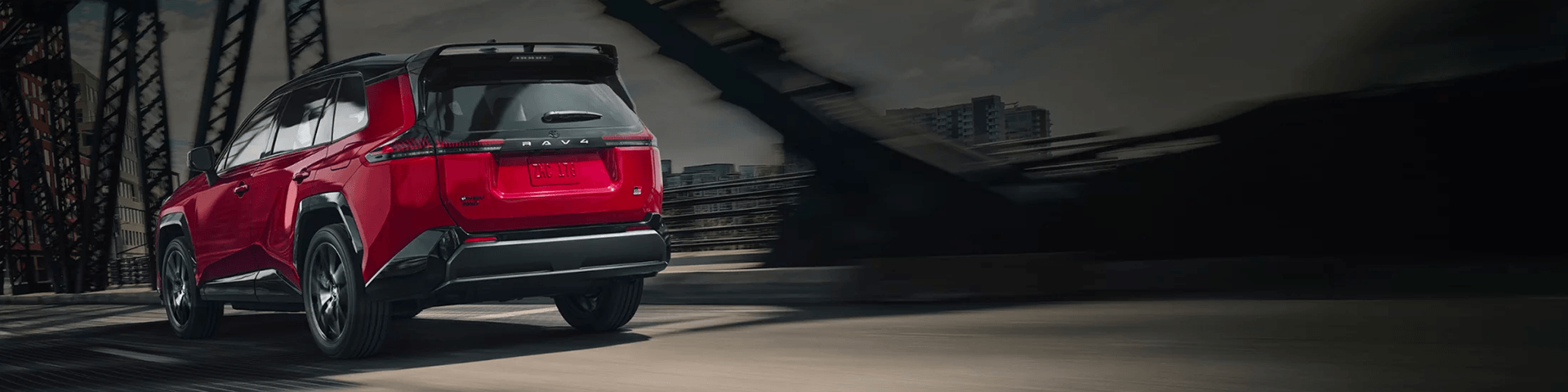 Rear view of a red SUV driving across a bridge with steel trusses, featuring a motion-blurred city background.