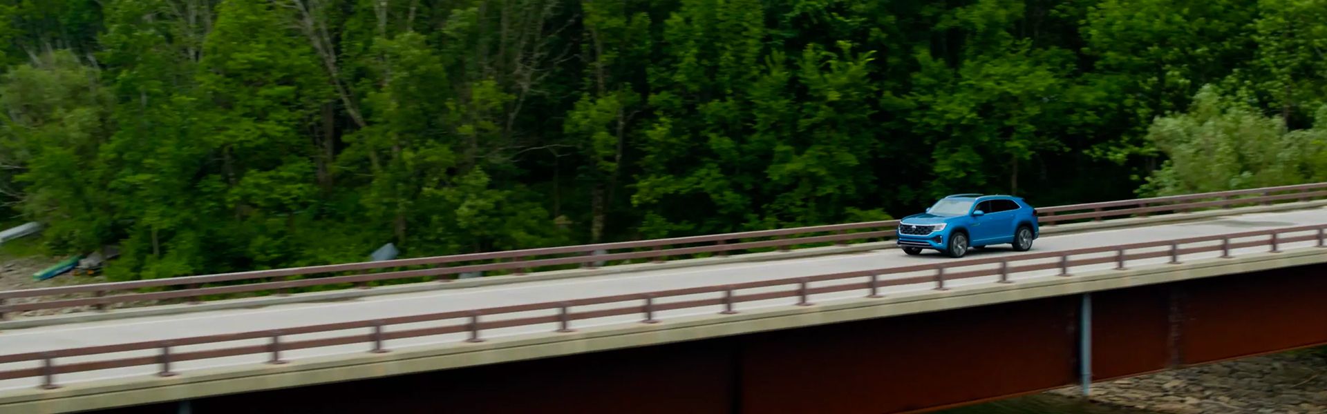 Blue SUV crossing a bridge surrounded by trees.