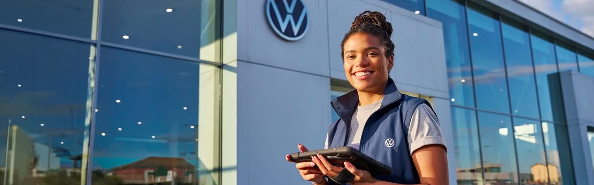 Smiling woman standing in front of a Volkswagen dealership.