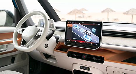 Tableau de bord intérieur d'un Volkswagen ID. Buzz montrant l'écran d'infodivertissement affichant les aides à la conduite (Travel Assist), avec une plage en arrière-plan.