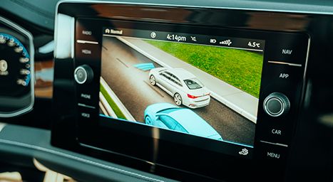Close-up of a car's infotainment screen displaying driver assistance features (a 3D view of two cars on a road).