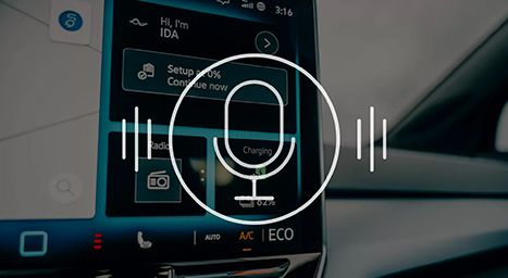 Gros plan sur l'écran d'infodivertissement d'une voiture affichant l'interface d'assistant vocal "Hi, I'm IDA" avec l'icône de microphone.