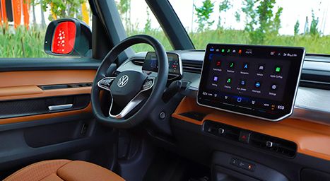 Interior dashboard of a Volkswagen ID. Buzz with brown trim and the steering wheel, showing the infotainment screen displaying app icons.