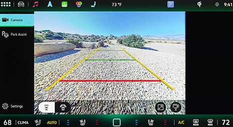 Infotainment screen showing a rear-view camera image with dynamic guidance lines (red, yellow, green) in a desert or rocky landscape.
