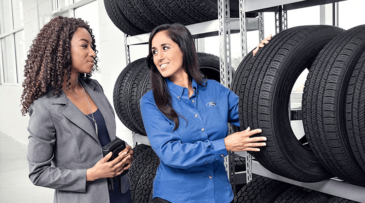A female service advisor showing a new tire to a customer in a bright showroom.