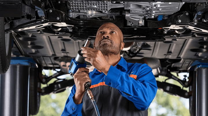 A professional mechanic using a power tool to work on the undercarriage of a car.
