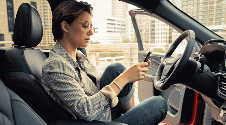 Une femme assise au volant d'une voiture utilisant son téléphone, garée en ville.