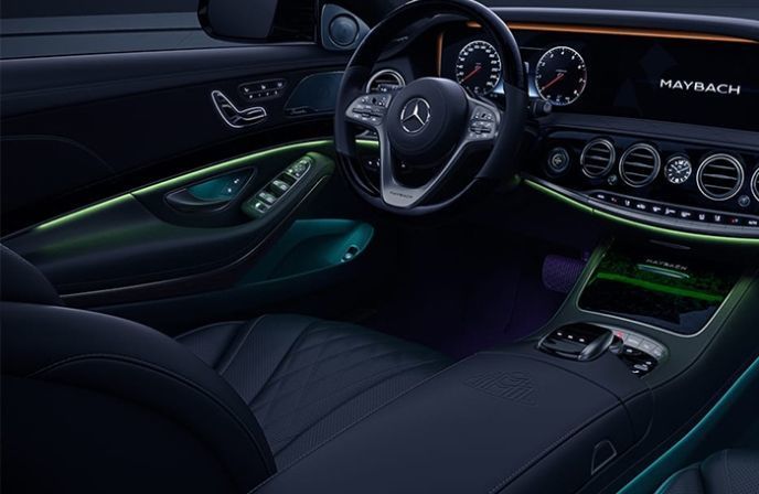 Luxury interior of a Maybach featuring a leather steering wheel and green and blue LED ambient lighting.