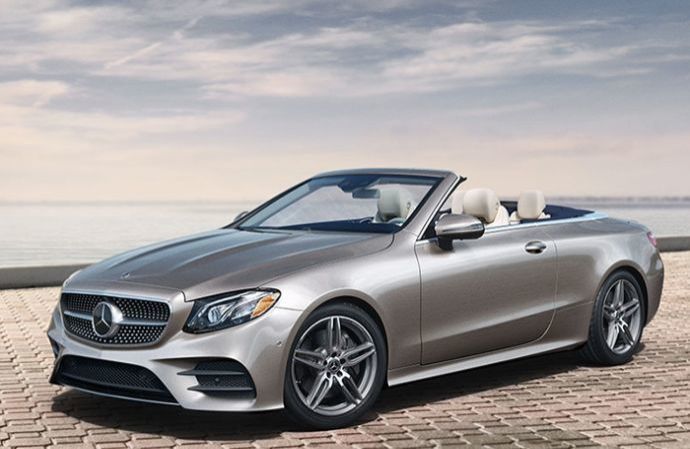 Une Mercedes-Benz cabriolet beige stationnée sur un pavé au bord de l'eau.