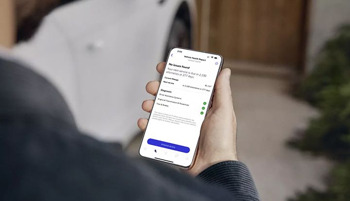 Close-up of a hand holding a smartphone that displays a myVW app Vehicle Health Report.