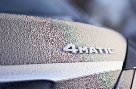 Close-up of the 4MATIC chrome badge on a car's frosted hood in winter.
