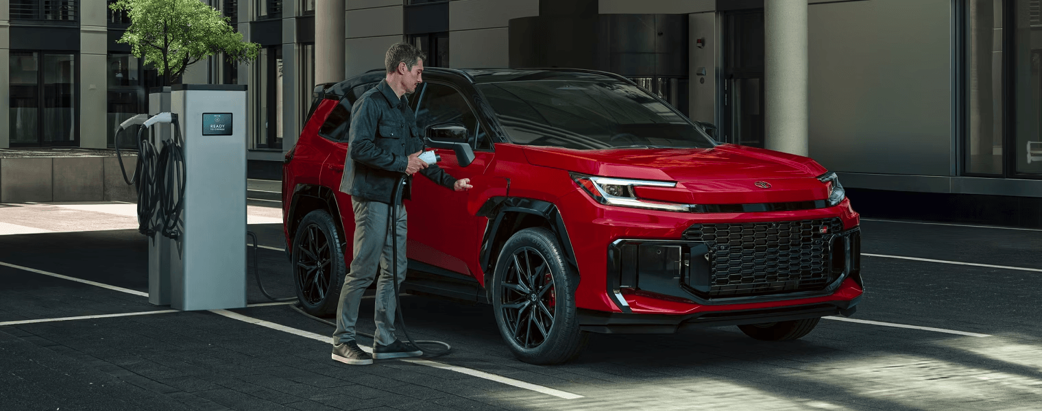 A man preparing to plug a charging cable into a bright red SUV at an outdoor electric vehicle charging station.