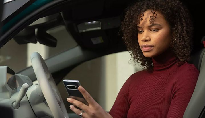 A woman sitting in the driver's seat of a car is looking intently at her smartphone.