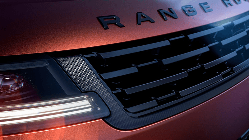Close-up of an orange Range Rover's front grille, featuring carbon fiber accents and a sleek LED headlight.