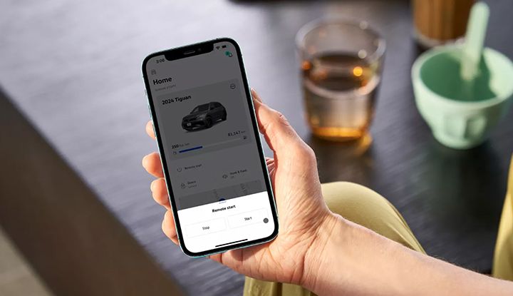 Gros plan sur une main tenant un smartphone affichant l'application myVW avec les options de démarrage à distance pour un VUS.
