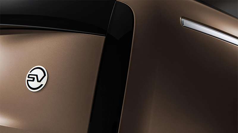 Close-up of the circular white and black "SV" ceramic badge on the rear of a bronze luxury SUV.