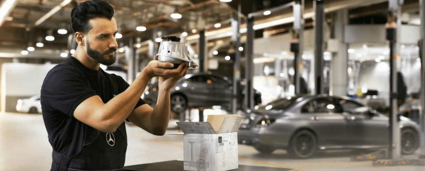 Un mécanicien examine une pièce automobile neuve dans un grand atelier de réparation.