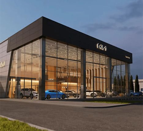 A modern, glass-front car dealership building at dusk, with several cars visible inside the showroom.