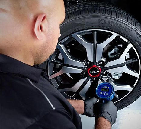A close-up shot of a mechanic checking the tire pressure on a Kia vehicle's wheel.