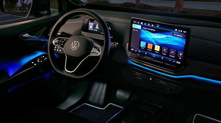 Night interior of a Volkswagen ID.4 showing the blue ambient lighting on the dashboard and doors, with the screen displaying the settings.