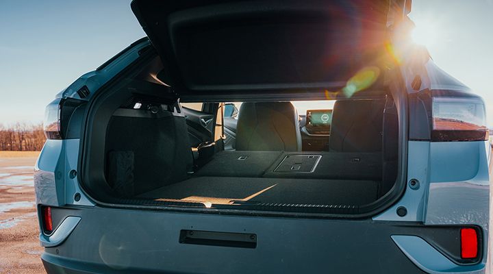 Rear view of a Volkswagen ID.4 SUV with the power tailgate open, showing the rear seats folded down under the sunset.