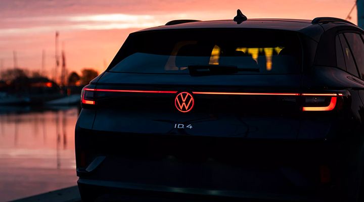 Rear view of a Volkswagen ID.4 SUV at twilight, showing the red illuminated VW logo on the tailgate.