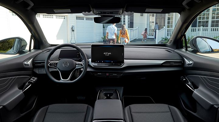 View of the interior of a Volkswagen ID.4 showing the dashboard and central screen, with a family in front of a house in the background.