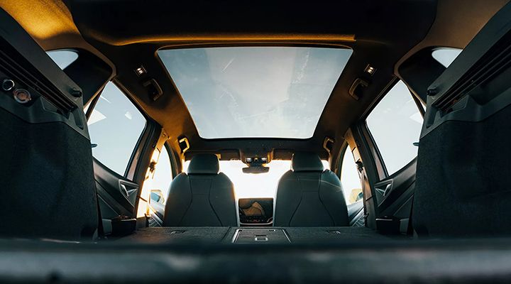 Vue de l'intérieur arrière d'un Volkswagen ID.4 montrant le toit en verre panoramique sous un ciel ensoleillé.