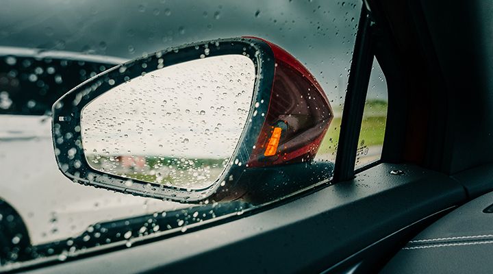Close-up of a side-view mirror covered in rain drops, with the turn signal indicator illuminated.