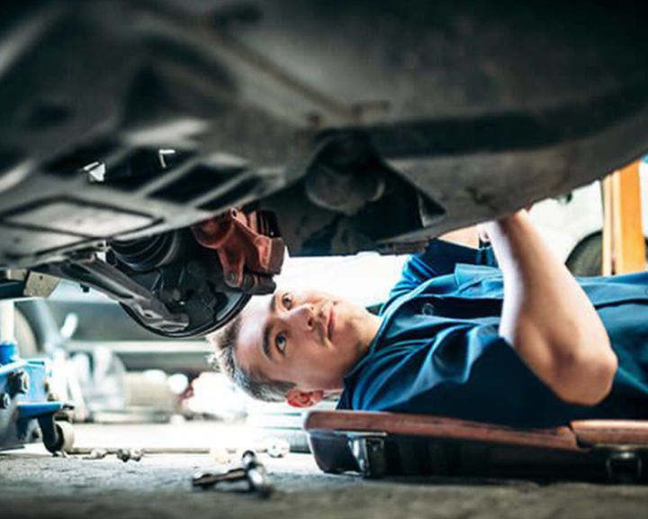 A mechanic lies on a creeper under a car, performing an inspection or repair.