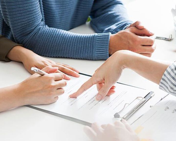 Close-up of a couple reviewing and signing vehicle financing documents with a consultant.