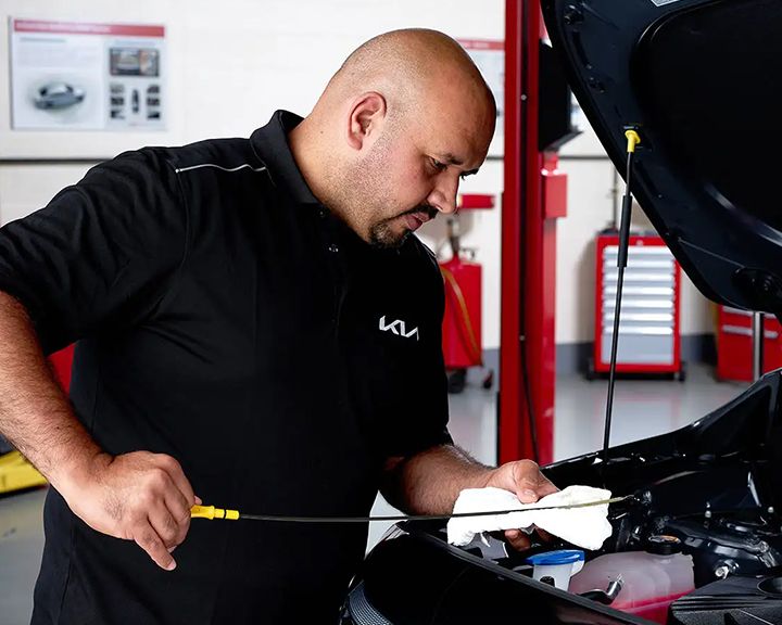A dealership mechanic in uniform checks a vehicle's oil level with a dipstick.