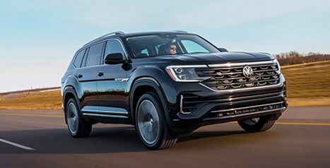 A black Volkswagen Atlas SUV drives on a rural highway under a clear blue sky.