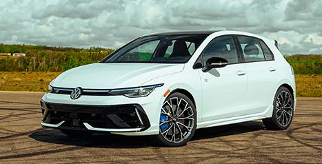 Three-quarter front view of a white Volkswagen Golf R with blue brake calipers, parked outdoors.