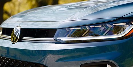 Close-up of the LED headlight and Volkswagen logo on the front grille of a blue sedan.